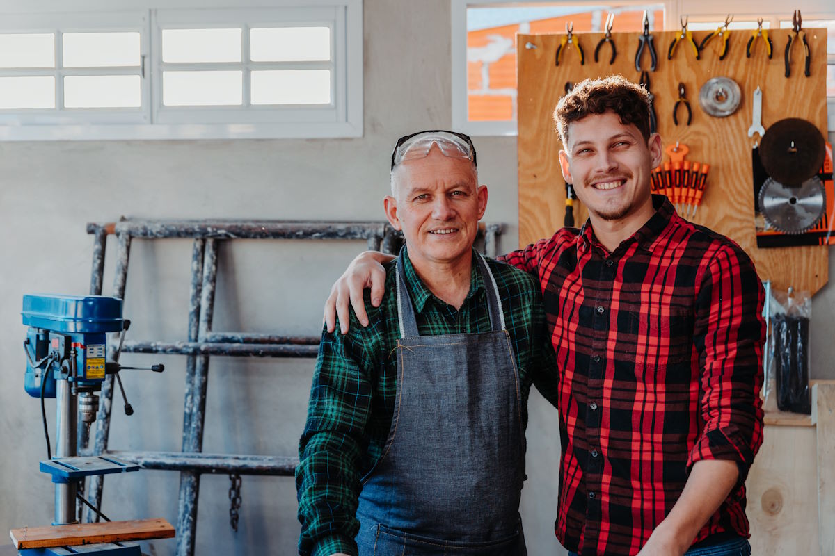 A senior carpenter hugging his young student