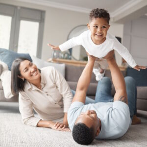 A happy mixed race family of three relaxing on the lounge floor and being playful together. Loving black family bonding with their son while playing fun games on the carpet at home