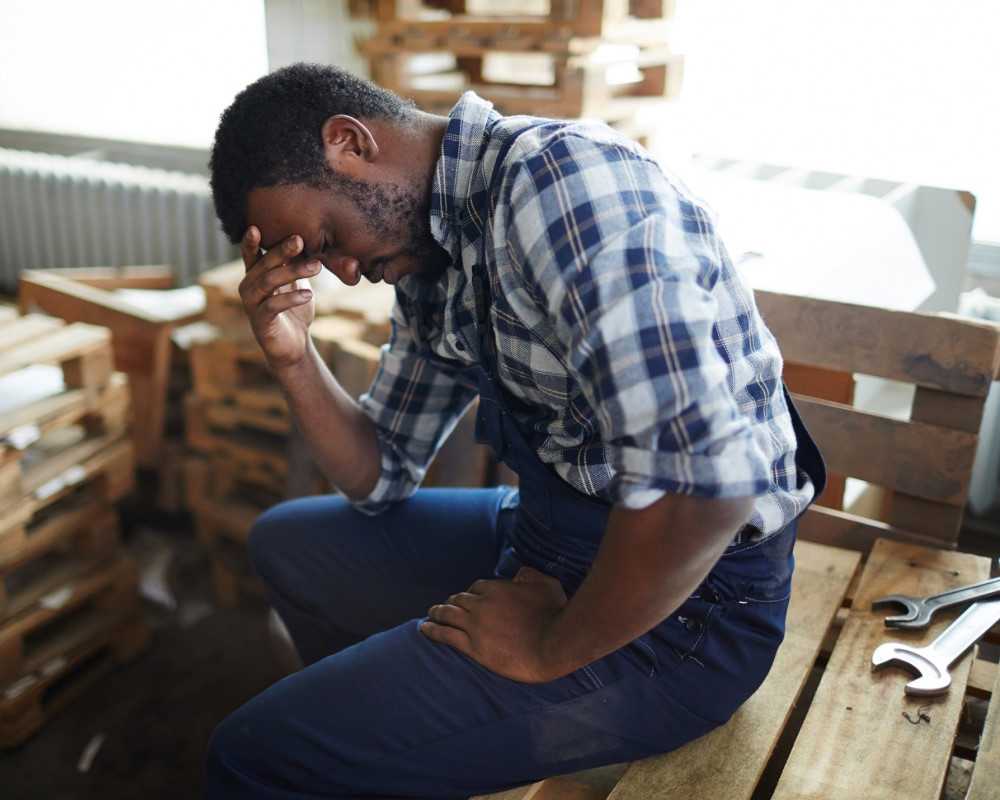 Photo of man sitting in workshop showing signs of stress